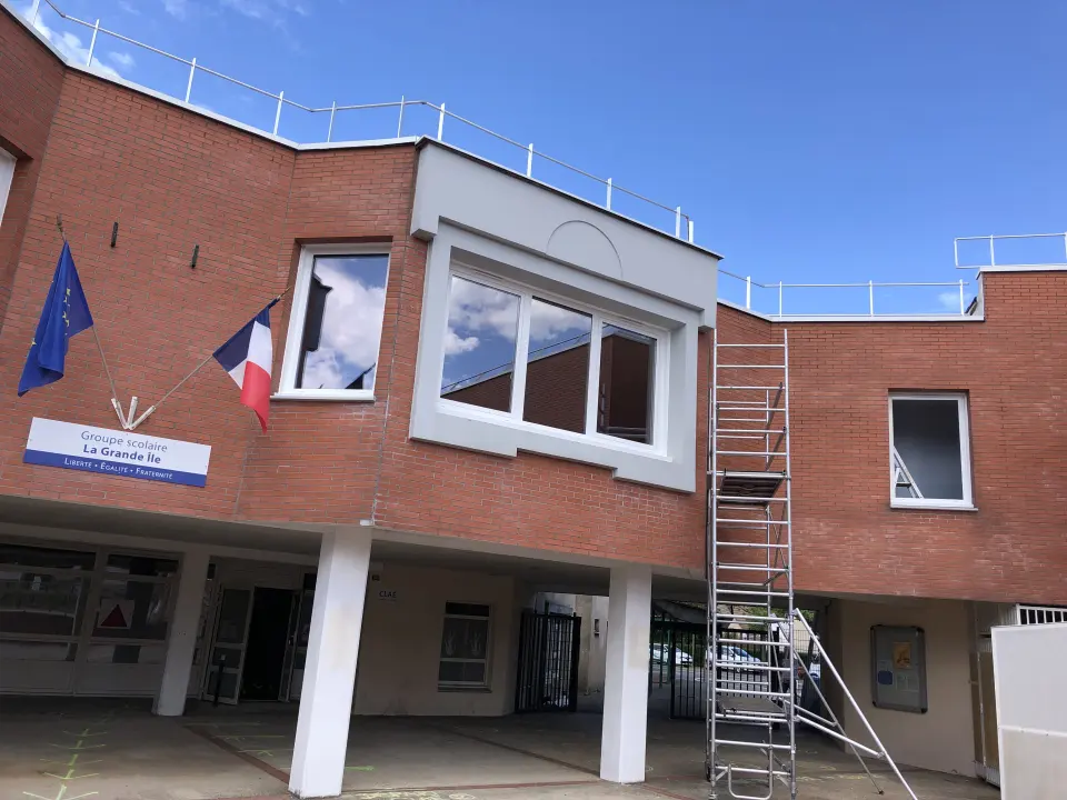 Façade en briques du groupe scolaire La Grande Île, fenêtres blanches à l'étage, échafaudage en place