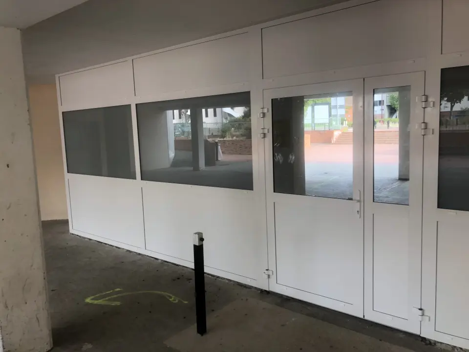 Cloison et porte vitrées blanches à l'entrée d'une école, sous un préau